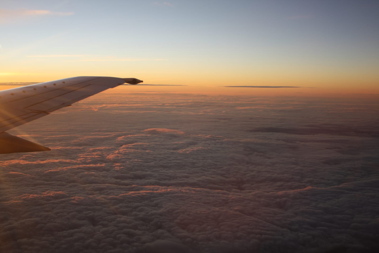 Tragfläche eines Flugzeugs über der Wolkendecke im Morgenlicht