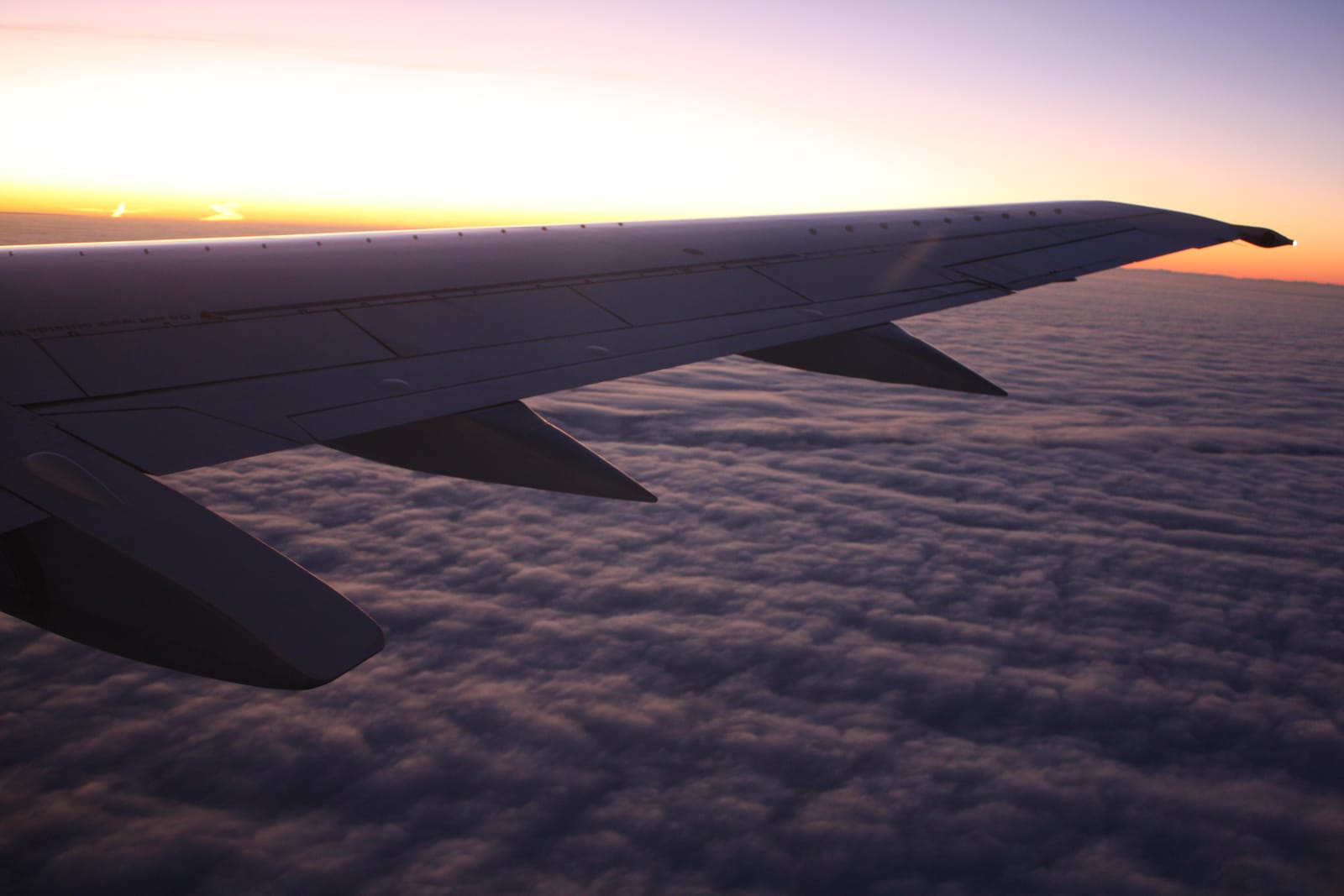 Tragfläche eines Flugzeugs über dem Wolkenmeer bei Sonnenaufgang