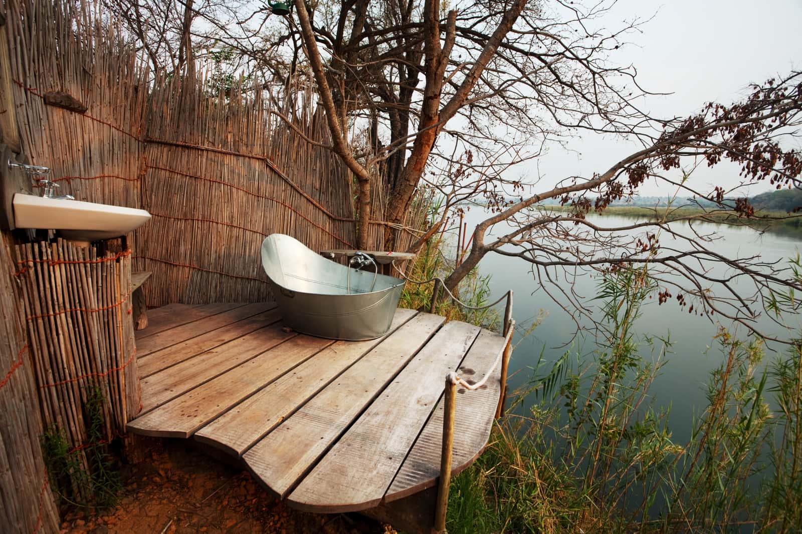 Freistehende Badewanne auf dem Holzdeck einer Safari-Lodge am Wasser